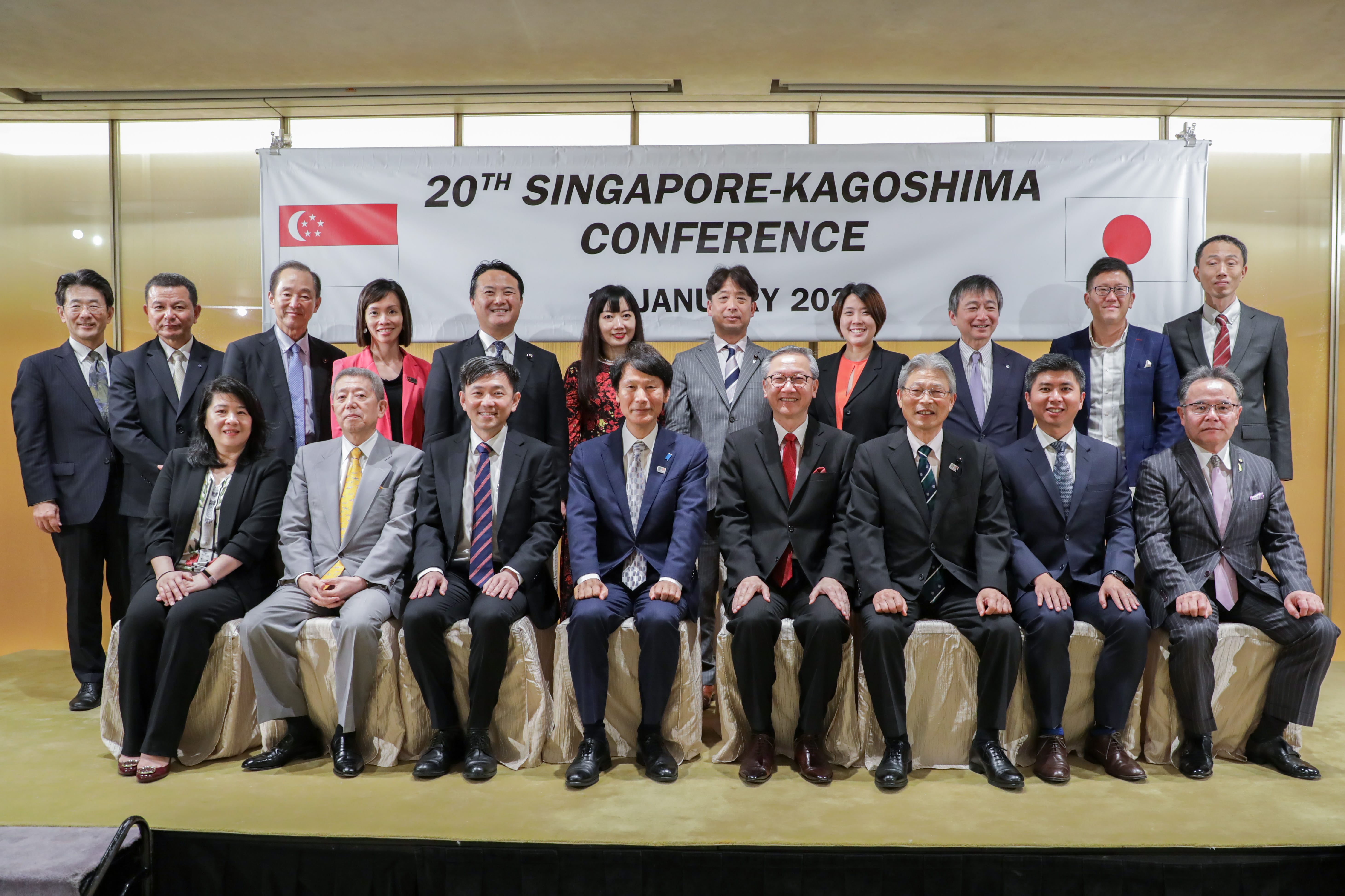 Group of people in business attire posing in front of a "20th Singapore-Kagoshima Conference" banner.